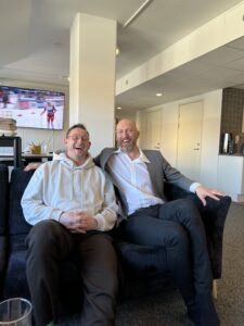 Daniel och Carl-Fredrik sitter nära intill varandra i en svart soffa, och skrattar mot kameran.